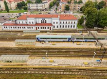 Widok z powietrza na dworzec i perony na stacji Ełk. Na jednym z peronów widać pociąg. W oddali widoczna zabudowa mieszkalna Ełku.