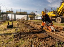 Widoczne są prace rozbiórkowe na stacji kolejowej w Białymstoku. W tle widoczna kładka dla pasażerów nad torami, pociąg i koparka.